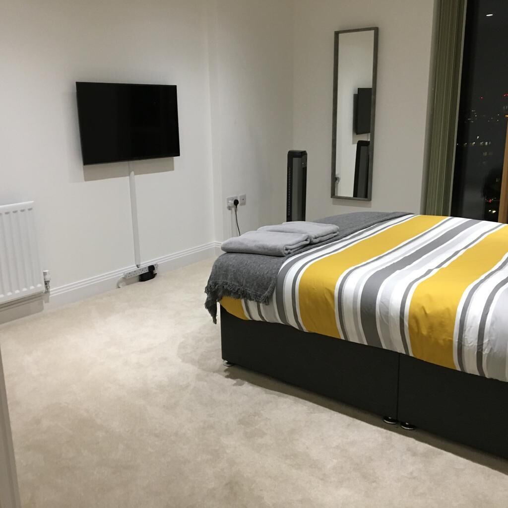 Un dormitorio moderno con cama, televisión de pantalla plana, espejo y radiador.