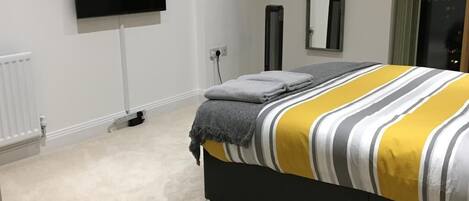 Un dormitorio moderno con cama, televisión de pantalla plana, espejo y radiador.
