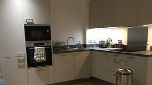 Ett modernt kök med vita skåp, en diskho i rostfritt stål och en inbyggd ugn.