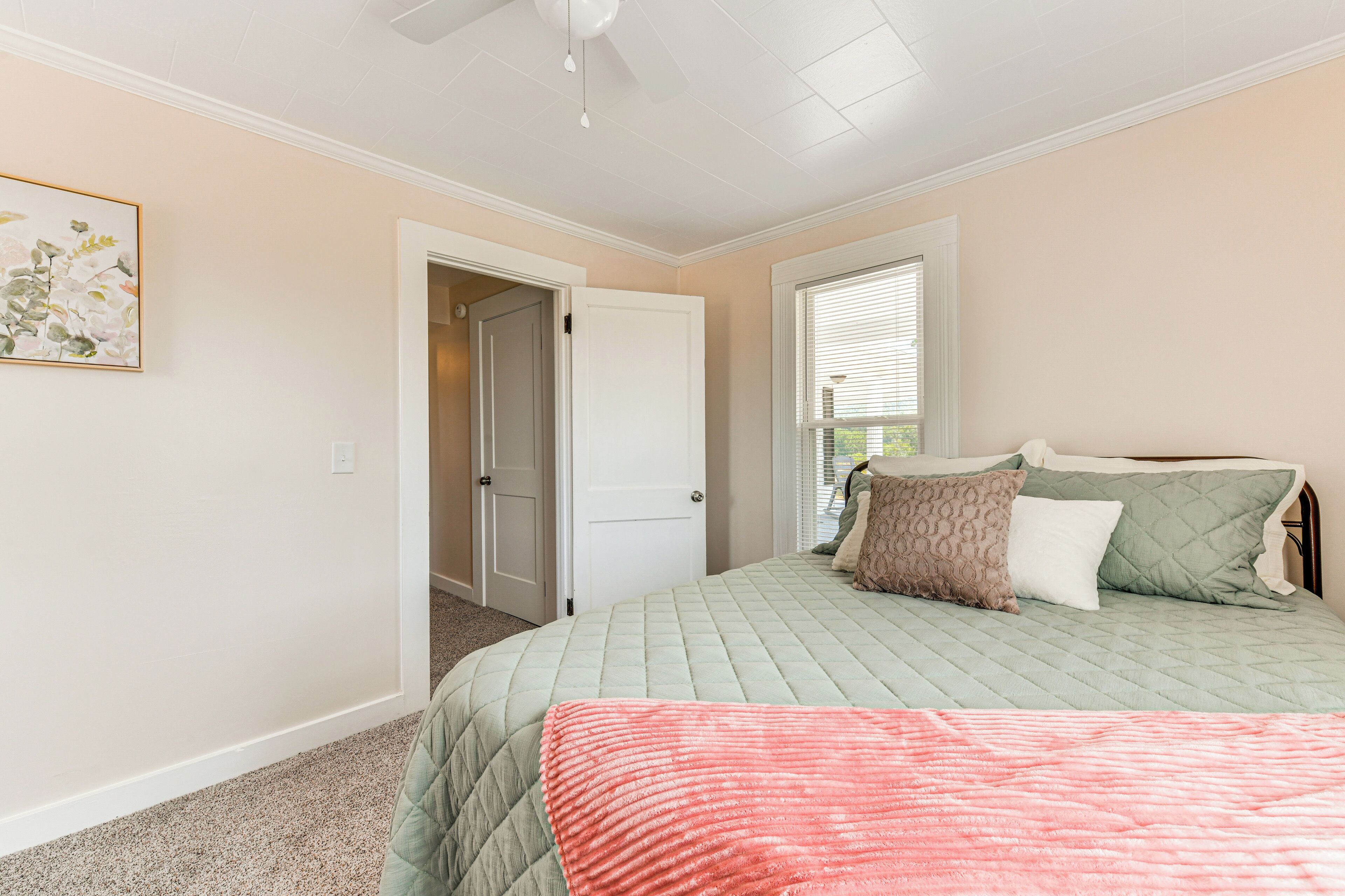 A bedroom with a bed, a door, a window, and a ceiling fan.