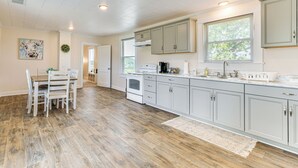 A spacious kitchen with white cabinets, a wooden floor, and a dining area with white chairs. - Peaceful Lenoir Home w/ Valley & Mountain Views! (Lenoir)