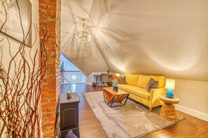 A cozy living room with a yellow sofa, a wooden coffee table, and a lamp. There is a brick wall and a ceiling with a unique design. - Walk to Dtwn: Colorful Cañon City Home w/ Grill! (Canon City)