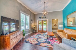 A living room with a flat-screen TV, wooden entertainment center, colorful rug, leather sofa, and a chandelier. - Walk to Dtwn: Colorful Cañon City Home w/ Grill! (Canon City)