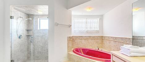 A modern bathroom with a glass-enclosed shower, a red bathtub, and a vanity with a mirror.