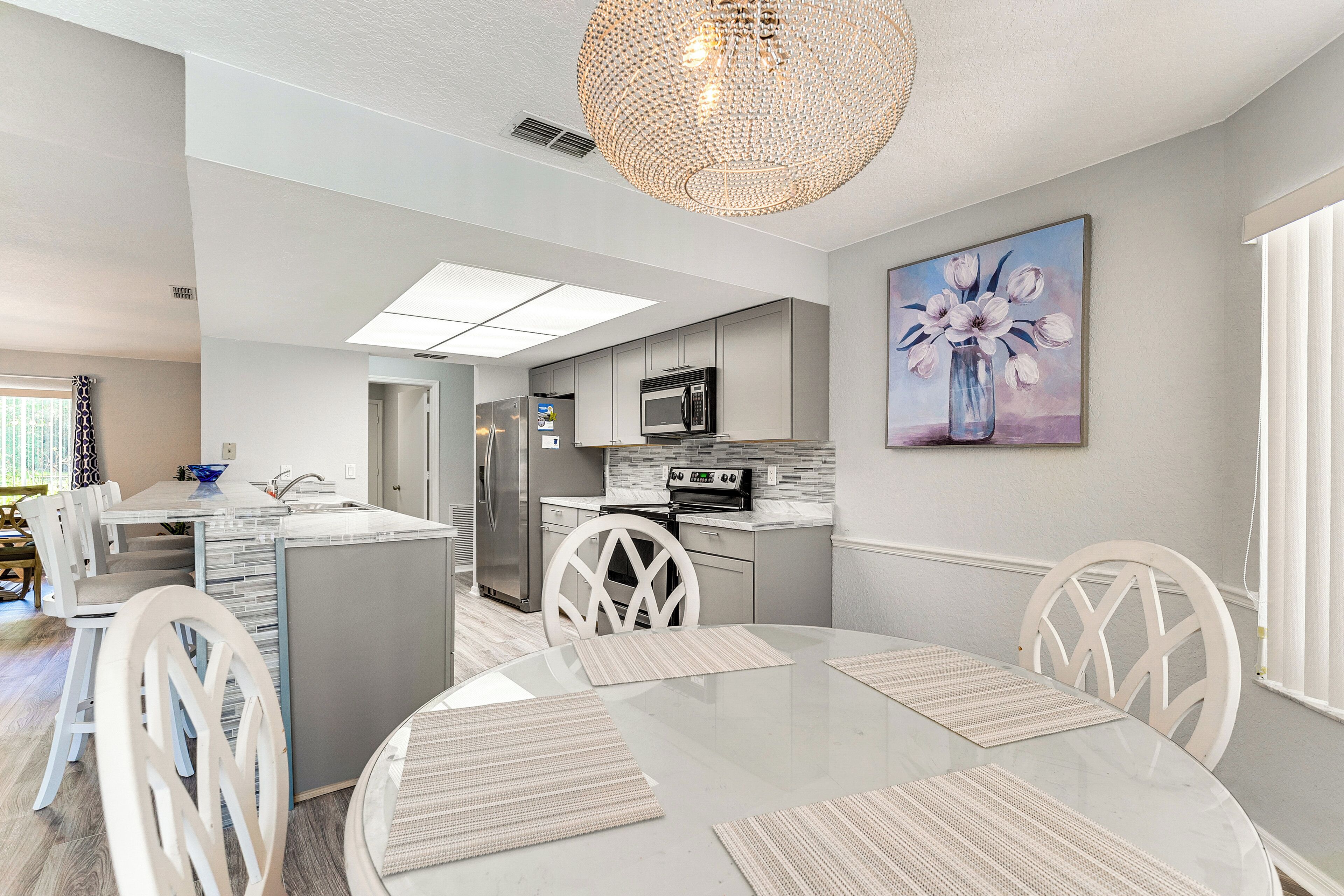 Een moderne keuken met een centraal eiland, witte kasten en een eetgedeelte met een ronde tafel en witte stoelen.