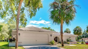A single-story house with a garage, surrounded by palm trees and a well-maintained lawn. - Spring Hill Home: Heated Pool, 9 Mi to Beach! (Spring Hill)