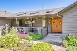 A house with a covered porch, a front door, and a small garden area with plants and a brick planter. - Spacious Camano Home w/ Hot Tub & Water Views! (Camano Island)