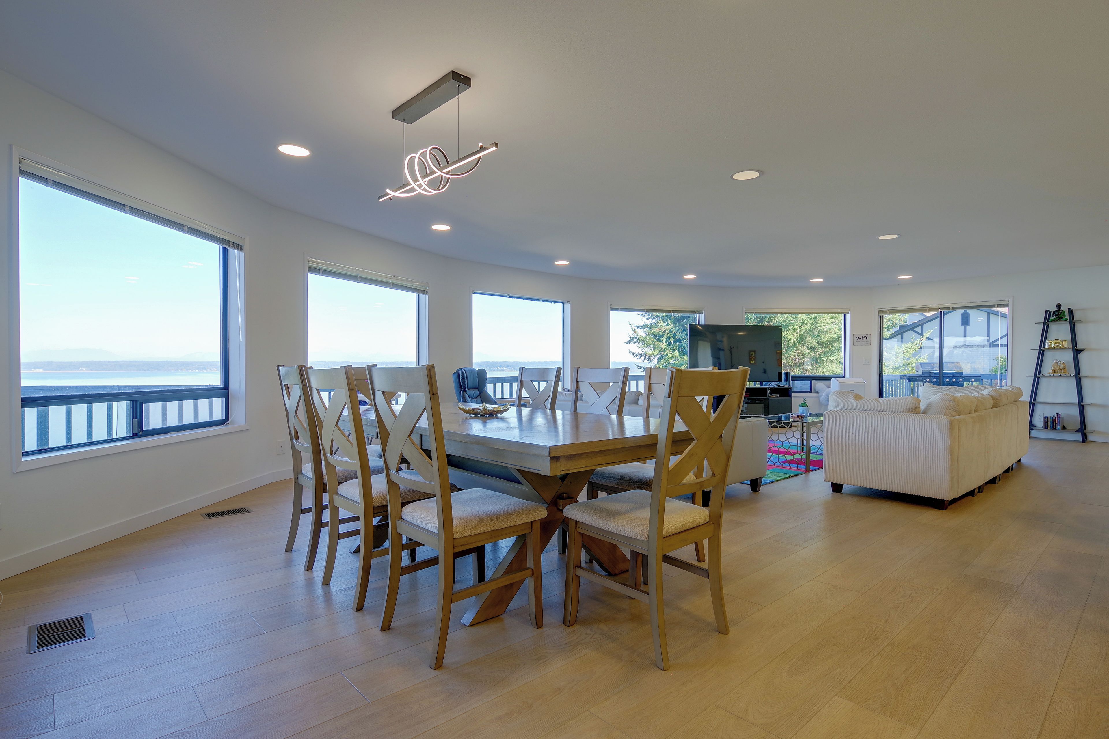 A spacious living area with a dining table and chairs, large windows, and a view of the outdoors.