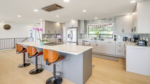 Una cocina moderna con una isla central, taburetes de bar, electrodomésticos de acero inoxidable y vistas al exterior.