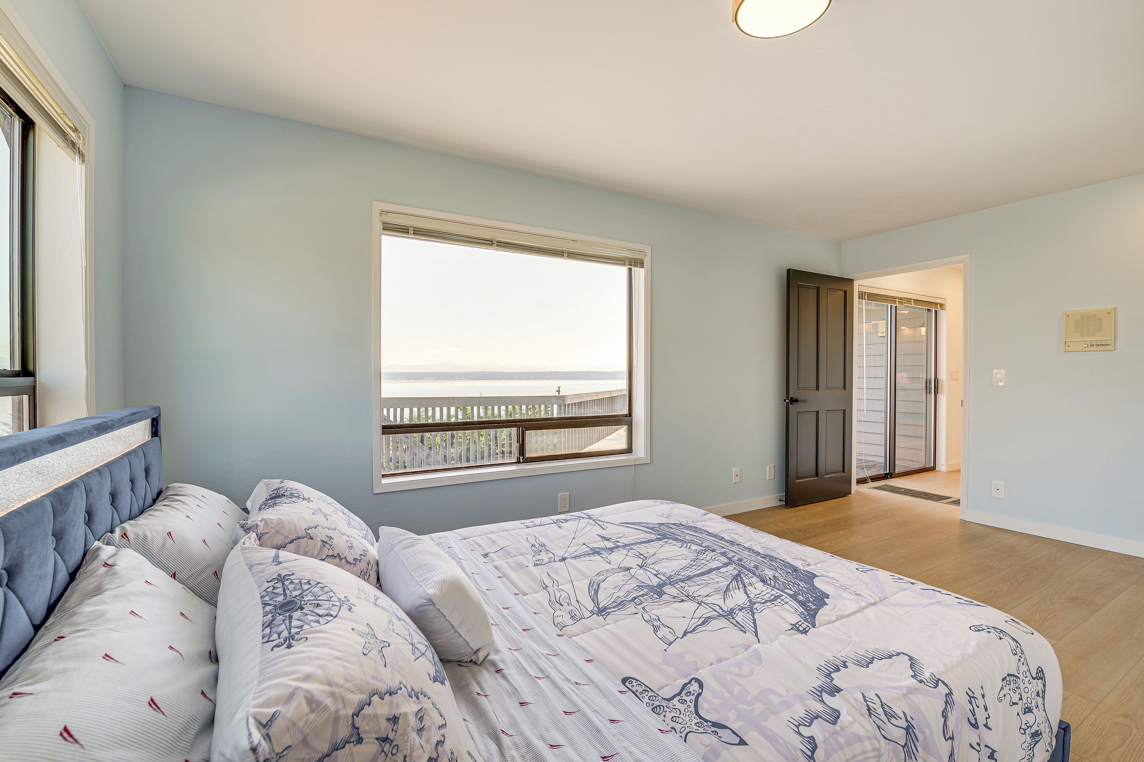 Une chambre à coucher avec un grand lit, une fenêtre donnant sur un beau paysage et une porte menant à une autre pièce.