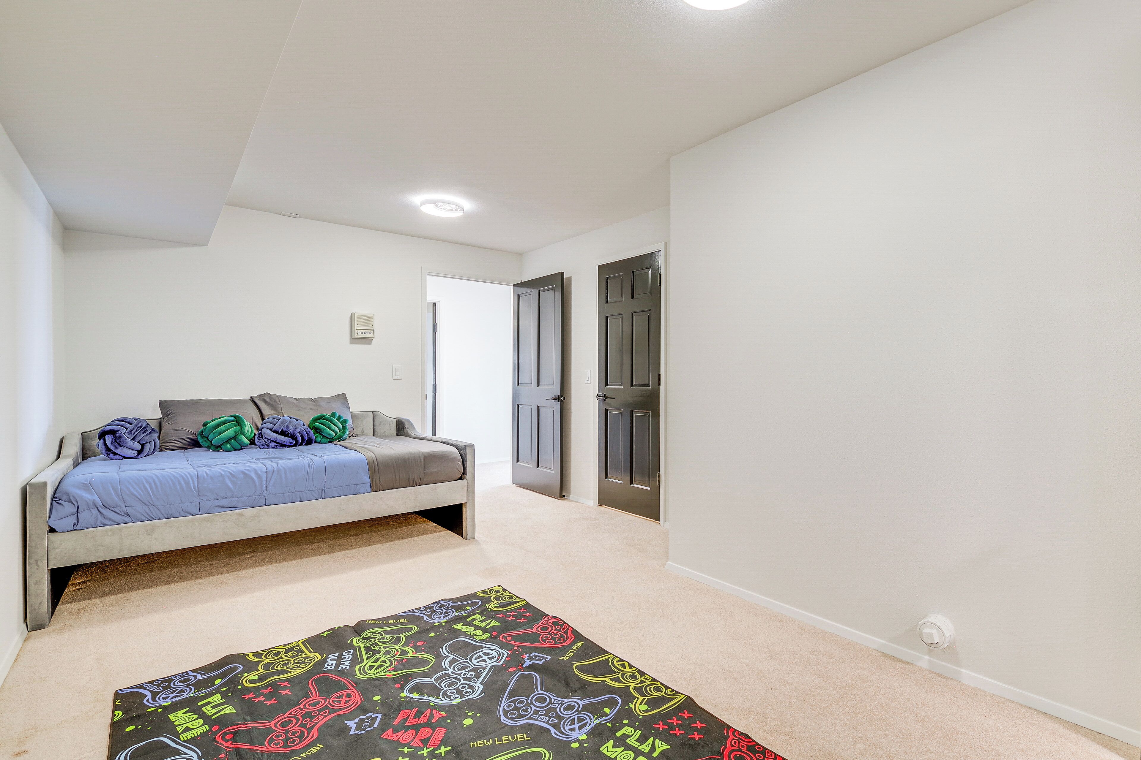 A bedroom with a bed, a carpet with gaming graphics, and two doors.