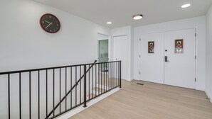 Een trap met een zwarte leuning die uitkomt op een plateau, een witte muur met een klok, en een deur met glas-in-loodramen.