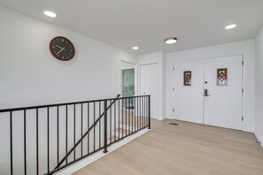 Un escalier avec une rampe noire menant à un palier, un mur blanc orné d’une horloge et une porte avec des vitraux.