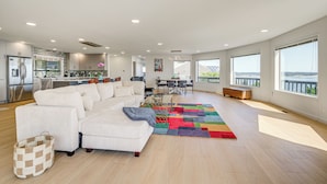 Un salón espacioso con un sofá blanco grande, una alfombra colorida y vistas de la ciudad a través de amplios ventanales.