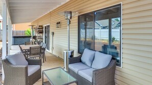 Een terras buiten met rieten meubels, een glazen tafel en een metalen heater.