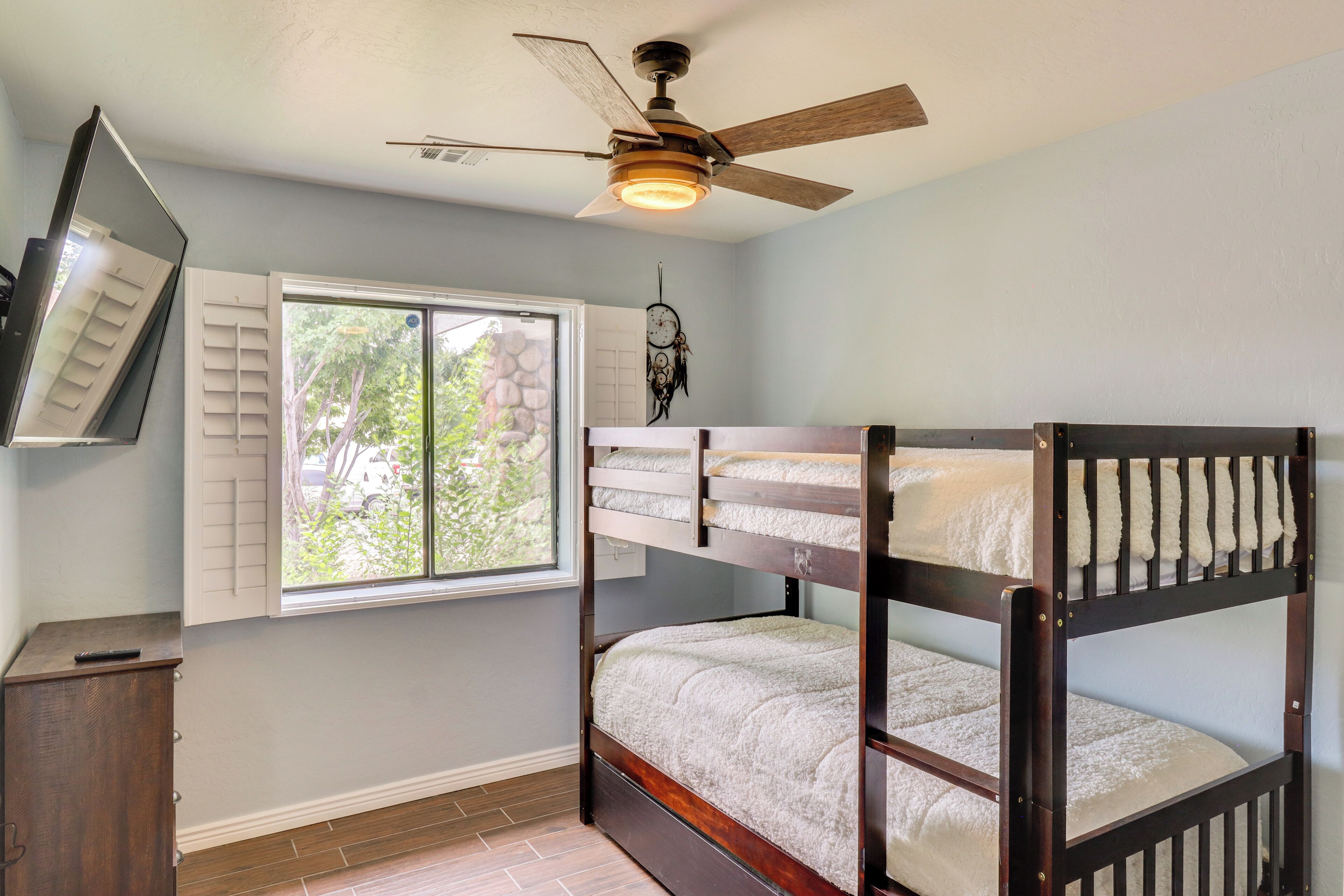 A bunk bed room with a ceiling fan, a window with shutters, and a dreamcatcher on the wall.