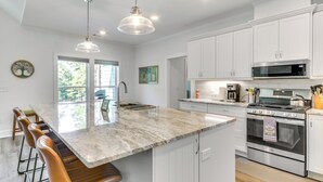 A modern kitchen with white cabinets, a large island with bar stools, stainless steel appliances, and pendant lighting. - Lakefront Mccormick Retreat w/ Patio & Views (McCormick)