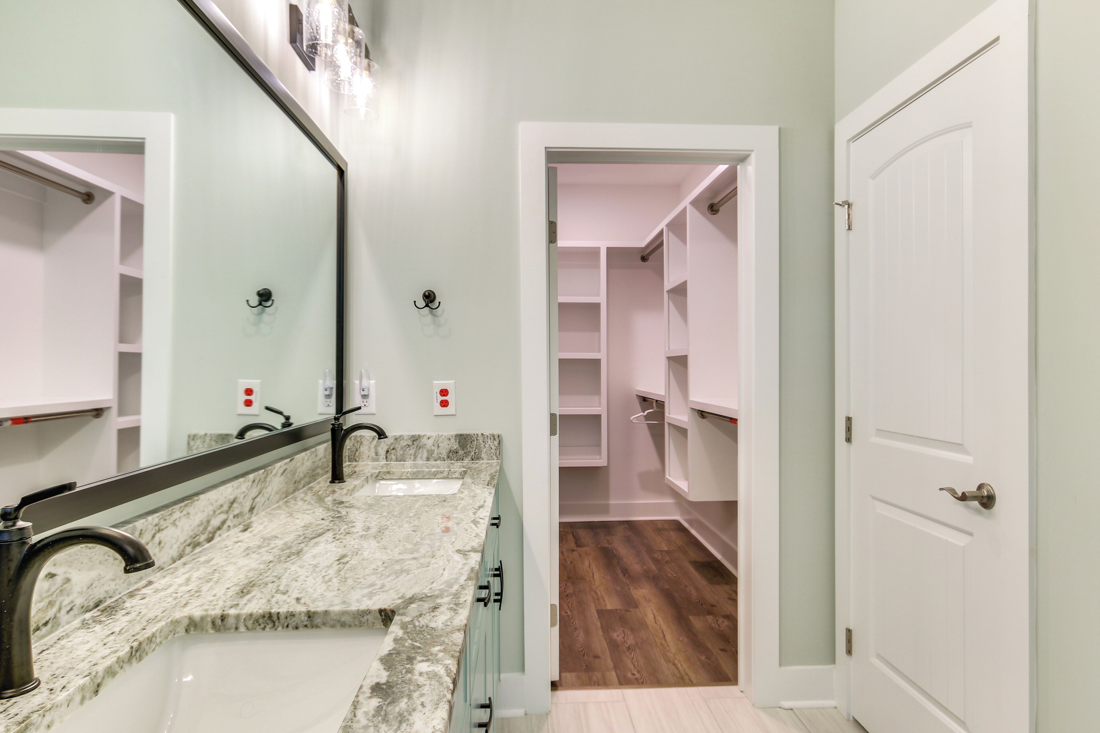 A bathroom with a marble sink, a mirror, and a walk-in closet with shelves.
