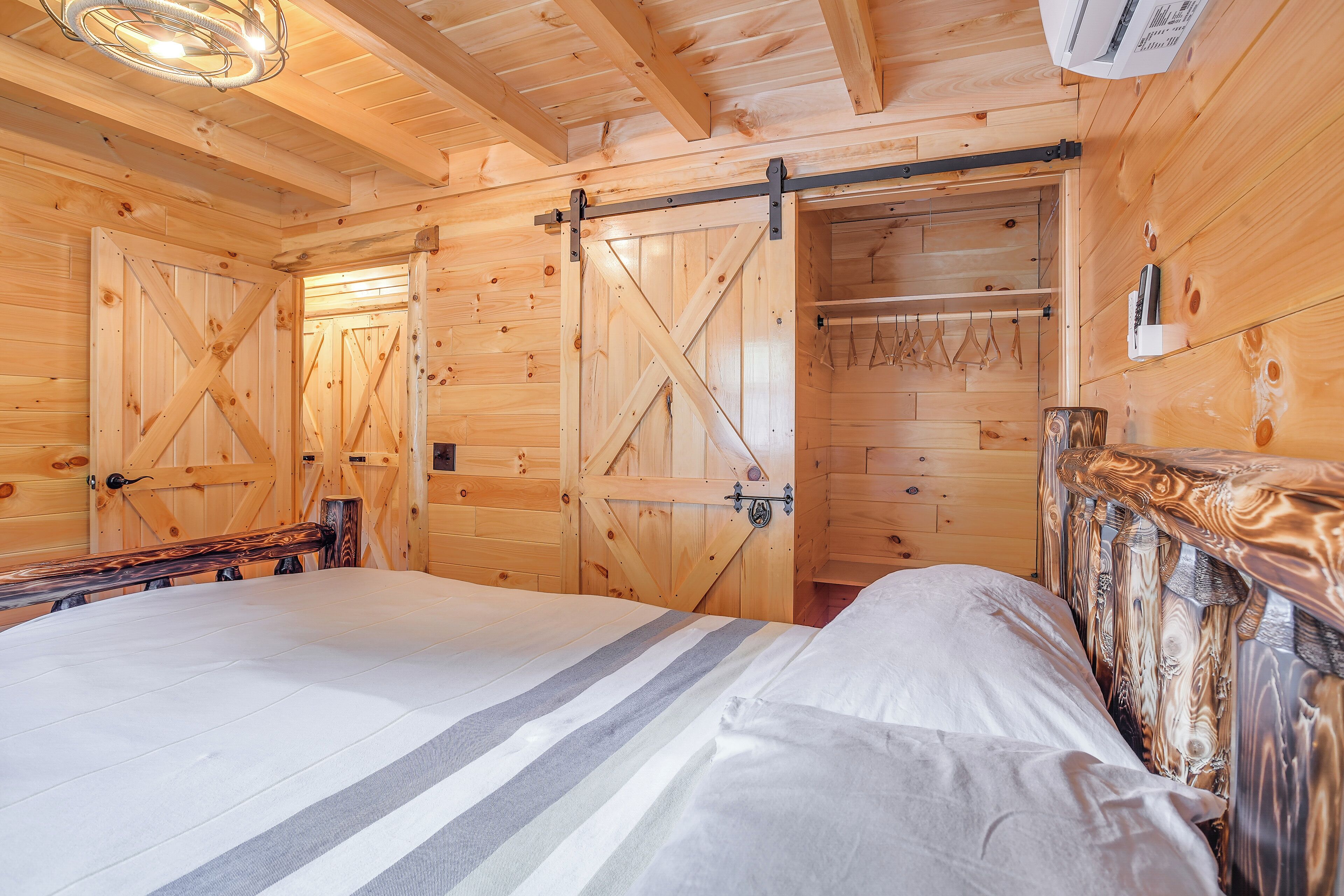 Una habitación tipo cabaña de madera con una cama, un armario de madera y una puerta corredera al estilo de granero.
