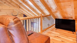 Un intérieur en bois avec un canapé en cuir, un téléviseur et une rambarde en bois.