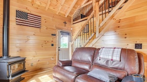 L’intérieur d’un chalet en bois, avec un canapé en cuir, un poêle à bois et un escalier.
