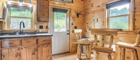 A wooden cabin interior with a kitchen area featuring a sink, cabinets, and a dining table with chairs.