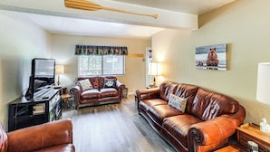 A living room with leather sofas, a wooden ceiling beam, a television, and a painting of a bear.