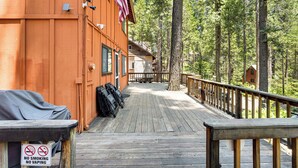 A wooden deck with a no smoking and no vaping sign, an American flag, and a view of the surrounding forest.