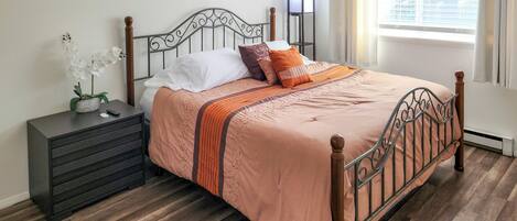 A neatly made bed with a wooden headboard, a bedside table with a lamp, and a potted orchid.