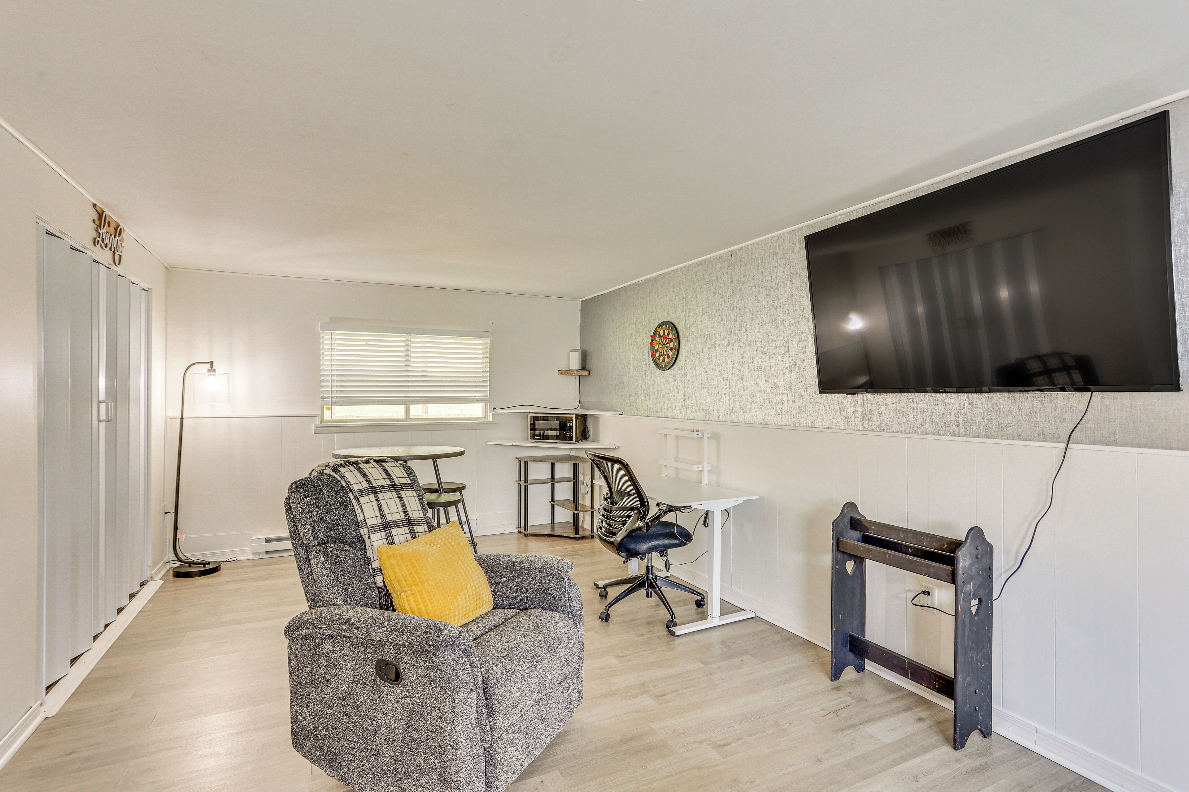 Una sala de estar moderna con un sofá gris, un cojín amarillo, una mesa de comedor y un televisor montado en la pared.