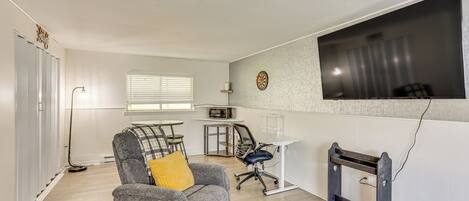 Una sala de estar moderna con un sofá gris, un cojín amarillo, una mesa de comedor y un televisor montado en la pared.
