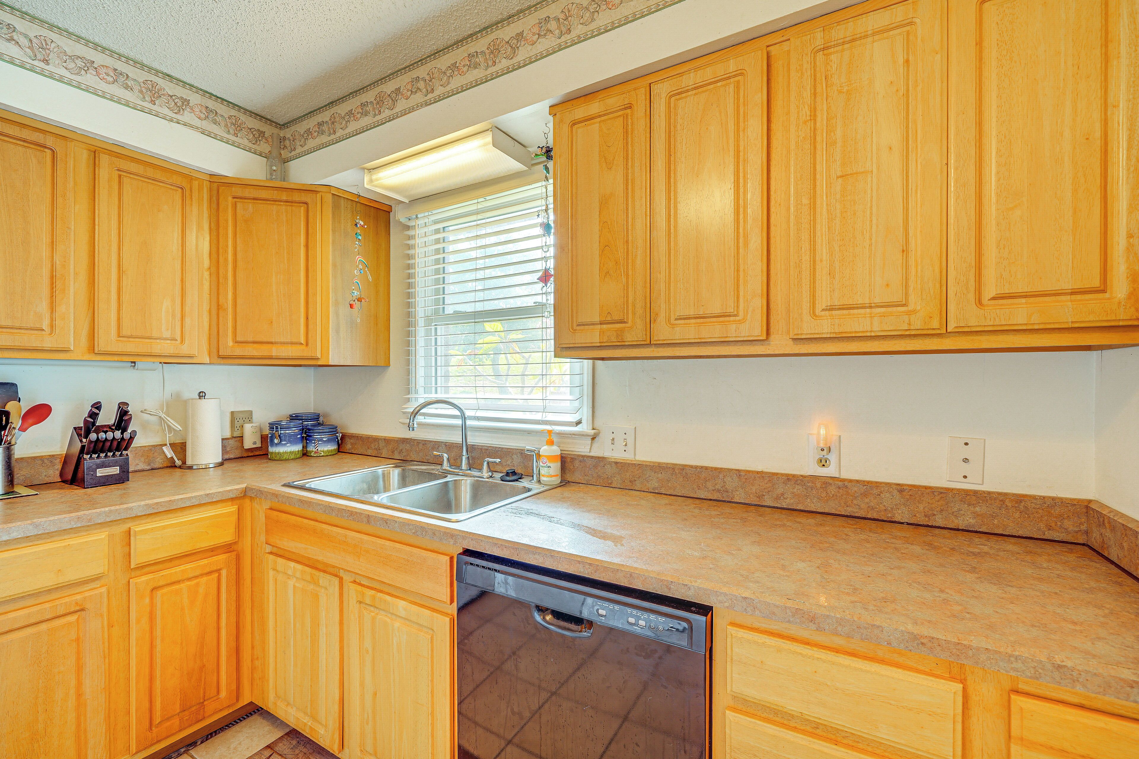 A kitchen with wooden cabinets, a stainless steel sink, a dishwasher, and a window with blinds.