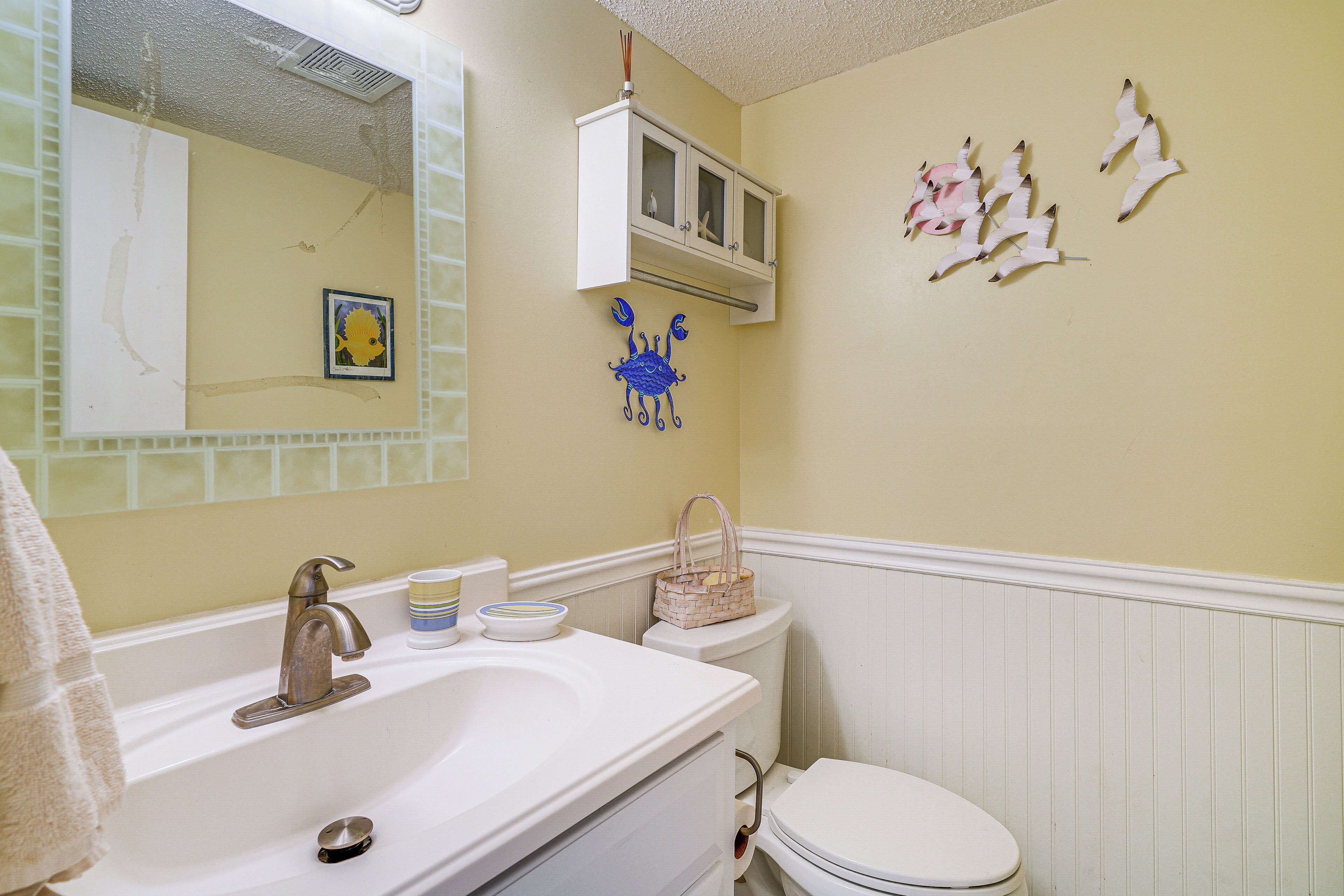 Un baño con lavamanos, espejo, inodoro y decoración en la pared.