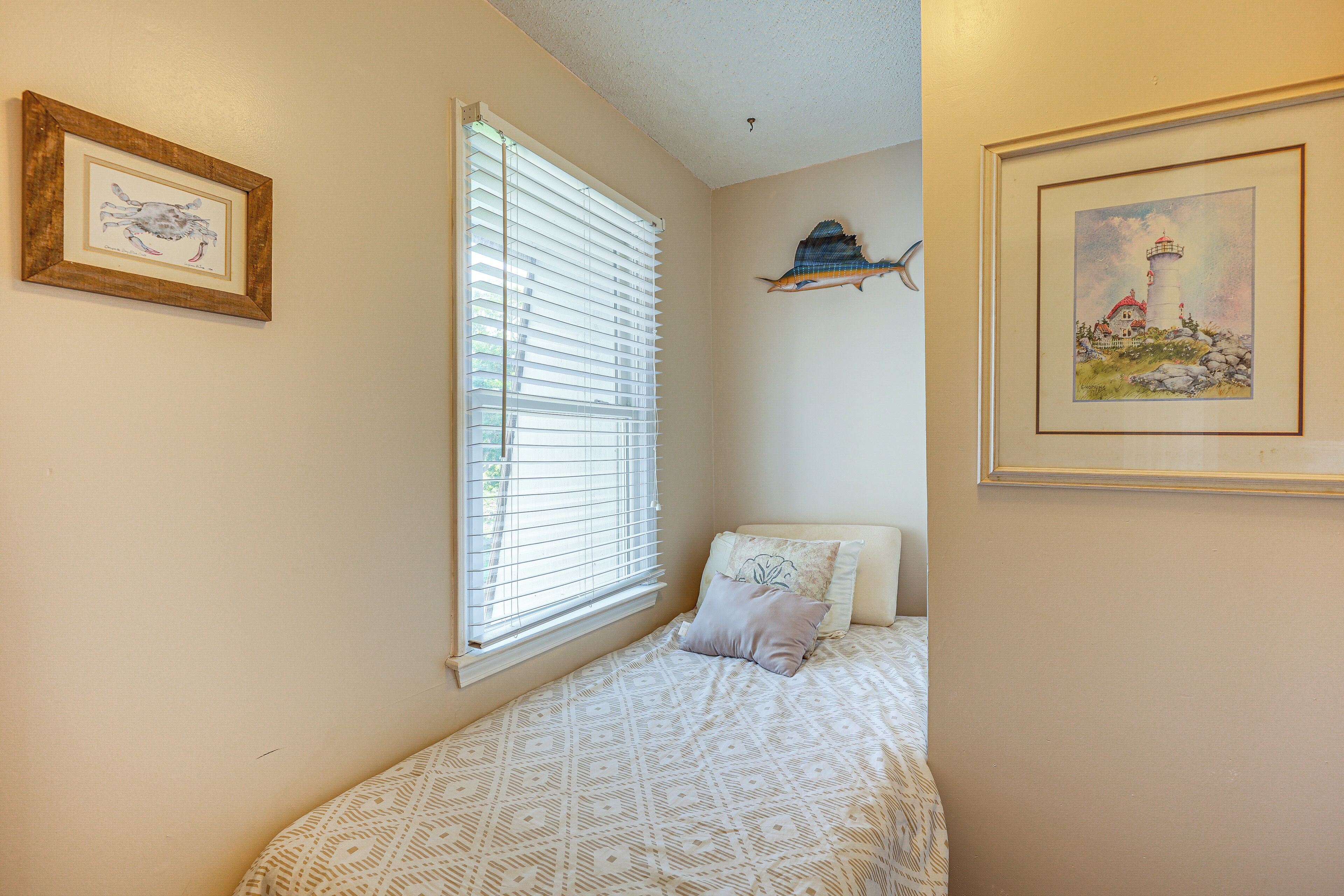 A bedroom with a bed, a window with blinds, and two framed pictures on the walls.