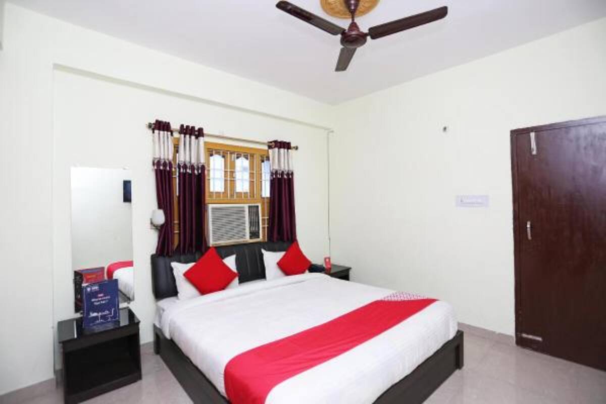 A hotel room with a bed, a ceiling fan, a window with curtains, a door, and a nightstand with a lamp.