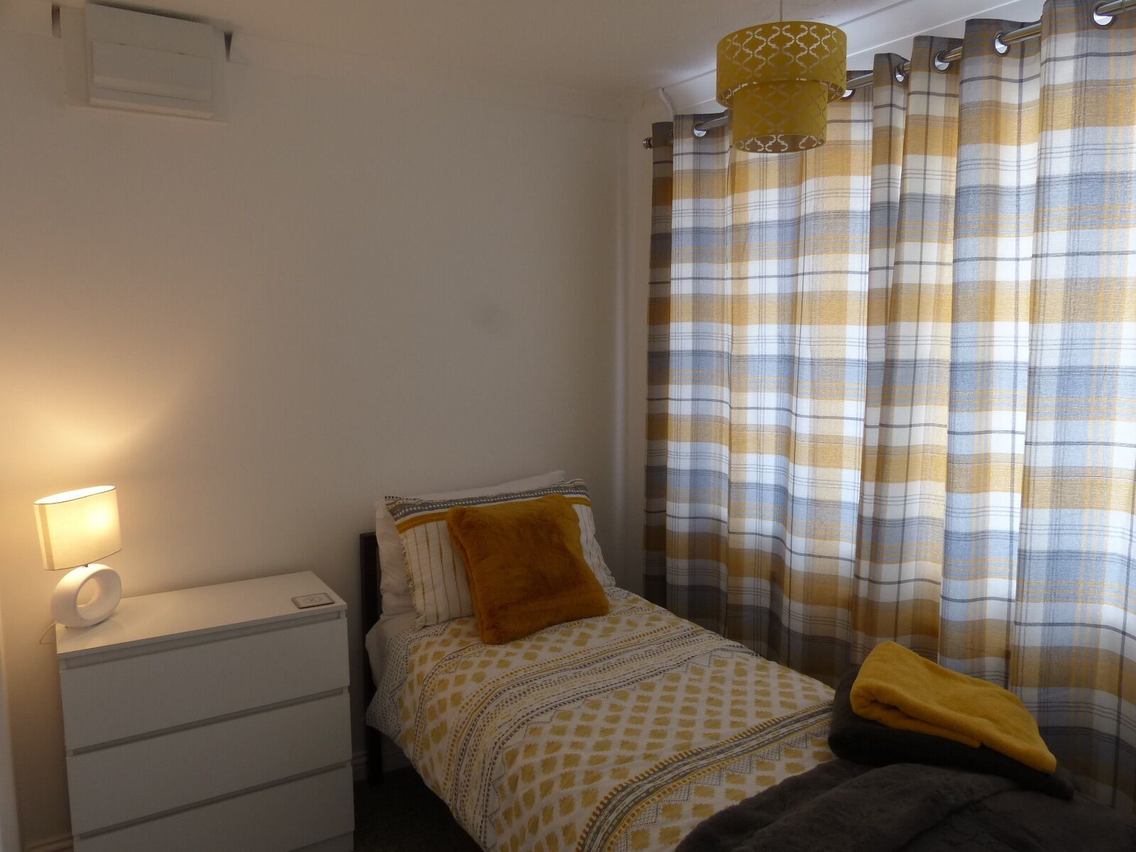 A bedroom with a bed, a bedside table, a lamp, and a window with curtains.