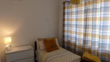 A bedroom with a bed, a bedside table, a lamp, and a window with curtains.