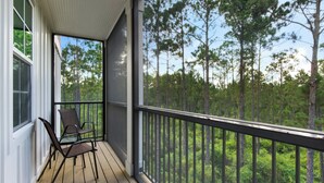 A wooden deck with two chairs and a railing overlooking a forest. - Pinewood Views: 2BR | 2BA, Sleeps 6 + Free Attraction Tickets! (Santa Rosa Beach)