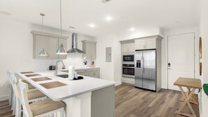 A modern kitchen with white cabinetry, stainless steel appliances, and a central island with seating. - Pinewood Views: 2BR | 2BA, Sleeps 6 + Free Attraction Tickets! (Santa Rosa Beach)