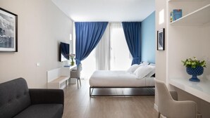 A modern hotel room with a bed, a desk, a chair, and a sofa.