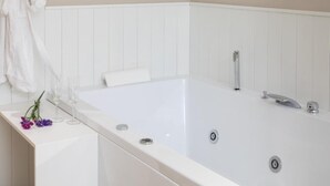 A white bathtub with a modern faucet, a towel, and a glass of water on a white countertop.