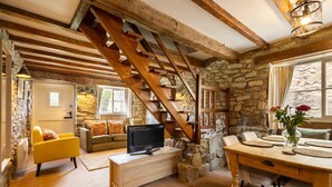 Ein rustikales Interieur mit einer Holztreppe, Steinwänden, einem gelben Sofa, einem Holzesstisch und einem Fernseher.