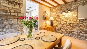 Ein rustikaler Essbereich mit Steinwand, Holzbalken, einem Holztisch mit gewebten Tischsets und einem Blumenstrauß.
