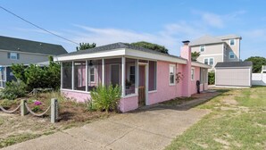 A pink single-story house with a covered porch, a chimney, and a small garden area. - The Pink House: Central Location | Pet-Friendly (Kill Devil Hills)