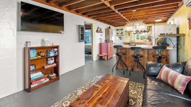 A spacious living area with a wooden ceiling, a large flat-screen TV, a bookshelf, a leather sofa, and a kitchen area with bar stools. - The Pink House: Central Location | Pet-Friendly (Kill Devil Hills)