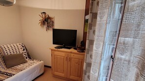 A cozy room with a patterned sofa, a television on a wooden cabinet, and a curtain with a heart pattern. - 2-room apartment for 4 people, pets and parking (Châtel)
