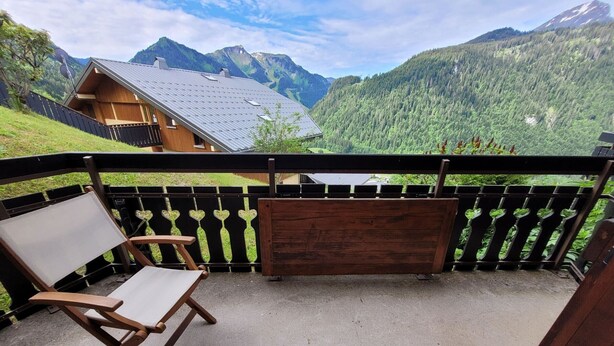 A balcony with a wooden chair and a wooden bench, overlooking a mountainous landscape with a house in the background. - 2-room apartment for 4 people, pets and parking (Châtel)