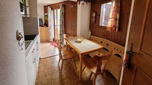 A cozy kitchen with wooden walls, a tiled floor, a dining table with chairs, and a window with curtains. - 2-room apartment for 4 people, pets and parking (Châtel)
