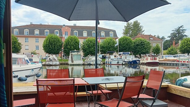 A terrace with tables and chairs, overlooking a canal with boats and buildings in the background. - Unique stay on Jupiter, comfortable boat in Digoin (Digoin)