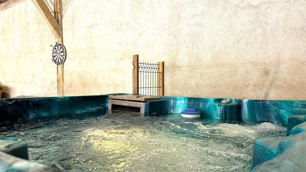 A hot tub with a wooden bench and a metal gate, surrounded by a stone wall. - Historic 1830 Mansion with Spa, Games, Pets Allowed (Jaligny-sur-Besbre)